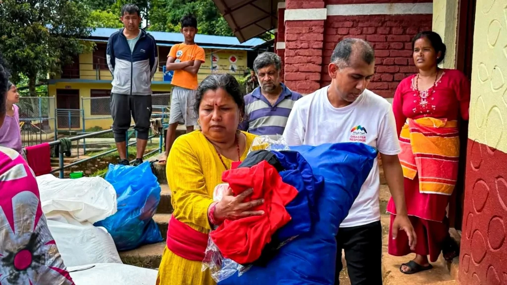 Volunteers carry colorful bundles of donated clothing outside a building as others watch, conveying community support and relief efforts in Nepal.
