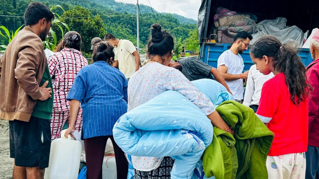 People unload donated bedding and clothing from a truck in a lush mountain village, conveying community aid, cooperation, and hope.