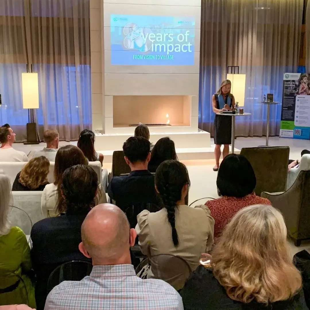 A woman stands at a podium, presenting to an engaged audience in a well-lit conference room in Hong Kong.