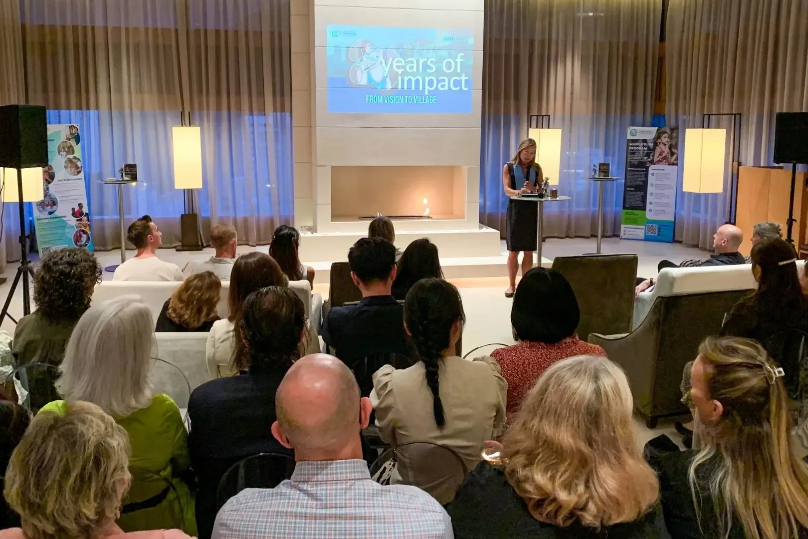 A woman stands at a podium, presenting to an engaged audience in a well-lit conference room in Hong Kong.