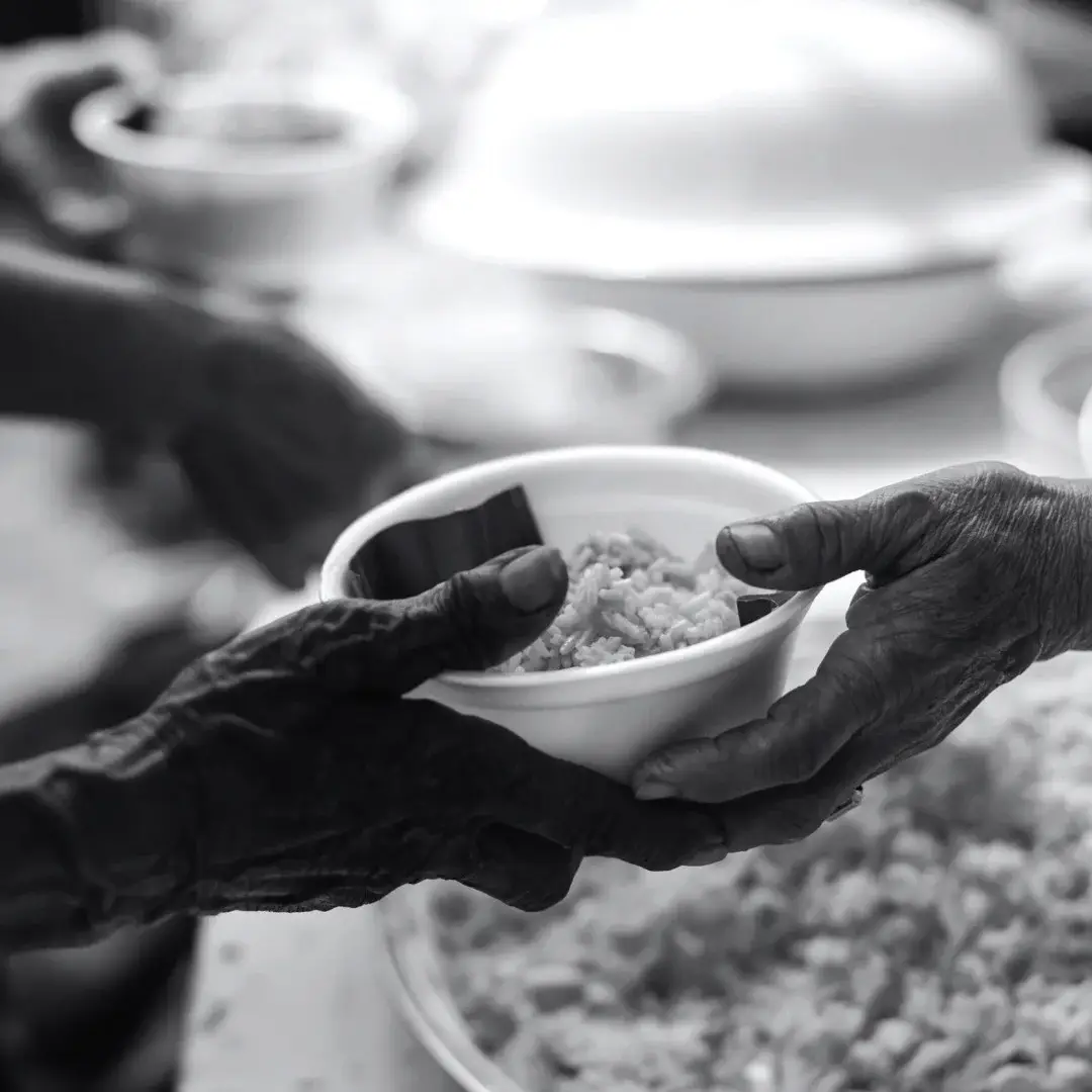 Black-and-white photo of hands passing a bowl of rice at a communal meal, conveying generosity, care, and shared nourishment.