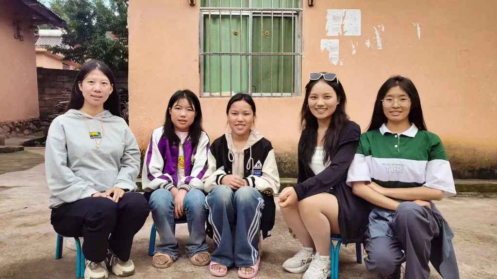 A group of five Asian women sitting on chairs in front of a rural structure in China.