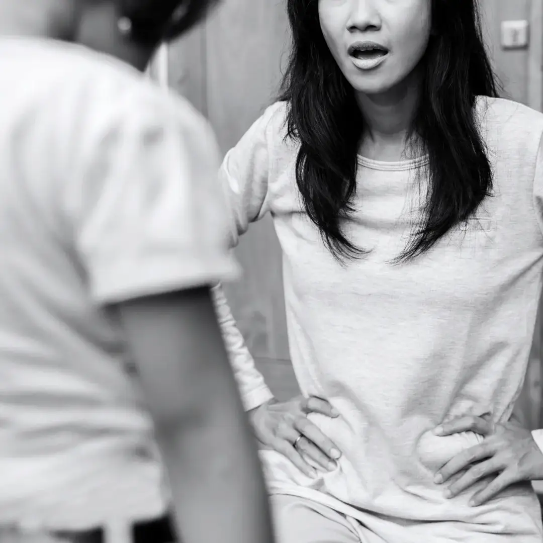 Black-and-white photo of a woman with hands on her hips speaking tensely to a child seen from behind, suggesting conflict or confrontation.