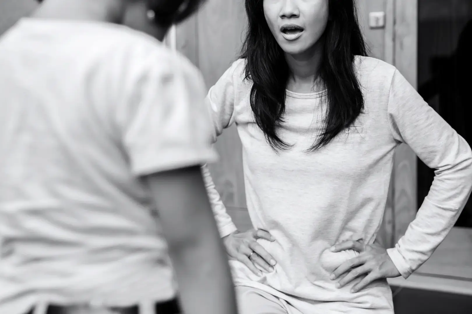 Black-and-white photo of a woman with hands on her hips speaking tensely to a child seen from behind, suggesting conflict or confrontation.