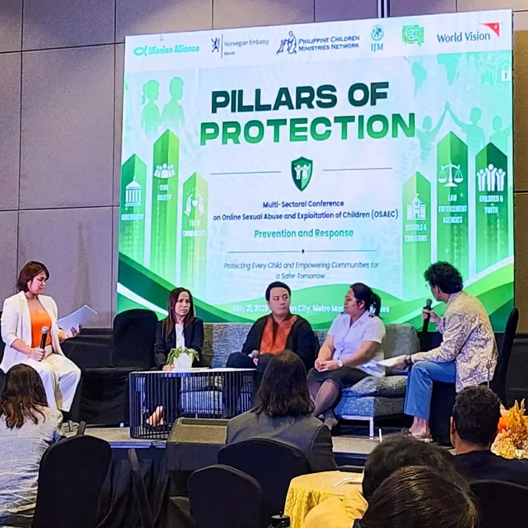 A panel of five speakers sits on a stage in front of a large screen titled Pillars of Protection at a conference about child safety and protection.
