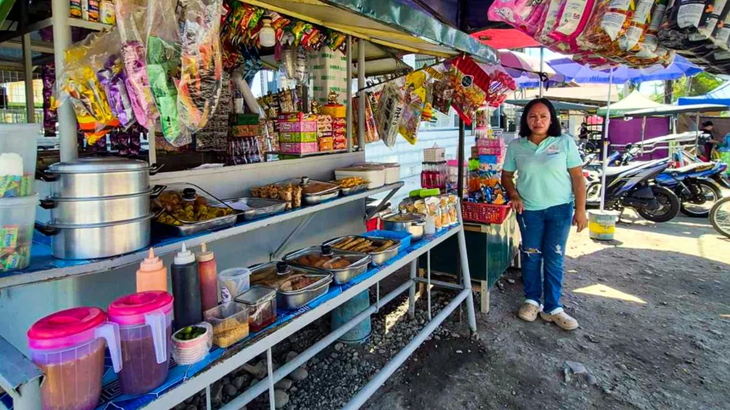 A woman stands in front of a colorful food stand in the Philippines.